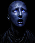 GRID THUMBNAIL — Close-up of a bald, blue-skinned figure with glowing blue eyes and parted lips, staring upward in fear against a black background.